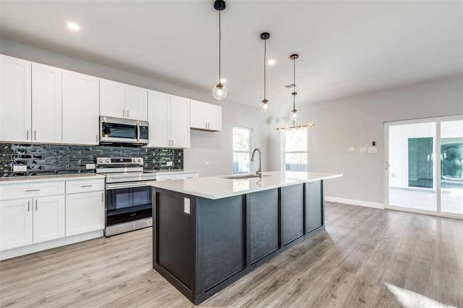 Kitchen featuring sink, white cabinetry, hanging light fixtures, stainless steel appliances, and a center island with sink