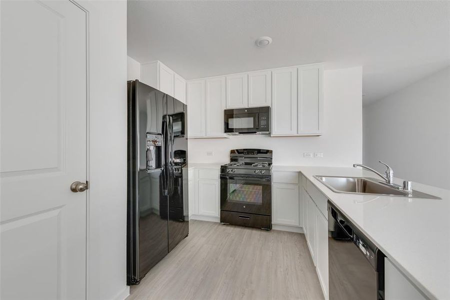 Kitchen featuring black appliances, light hardwood / wood-style floors, white cabinets, and sink