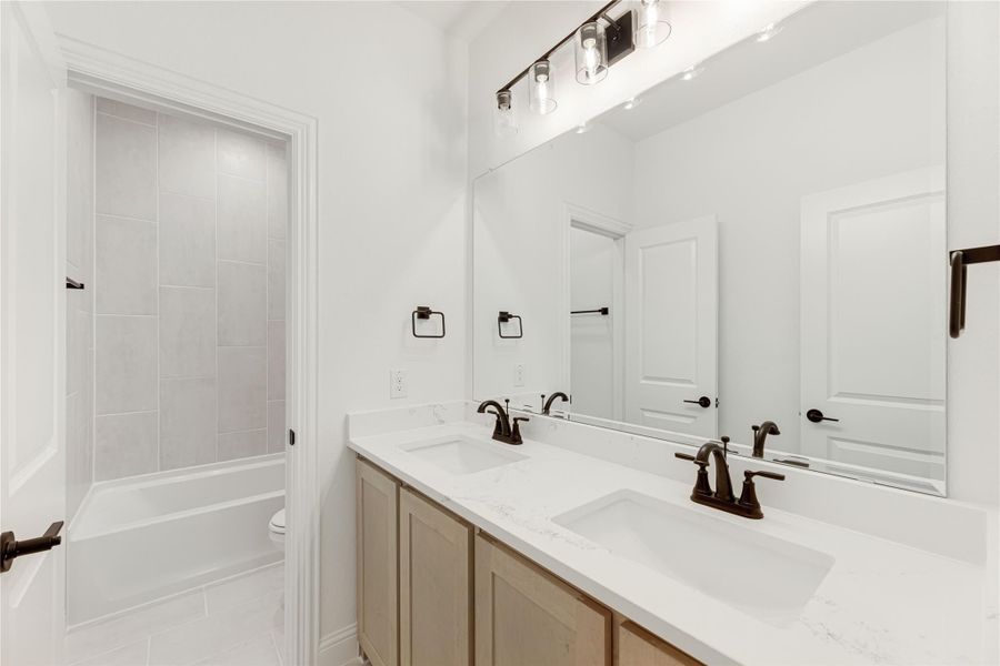 Bathroom with double sink vanity, white quartz countertop, and tiled tub-shower combo in background Bathroom with double sink vanity, white quartz countertop, and tiled tub-shower combo in background