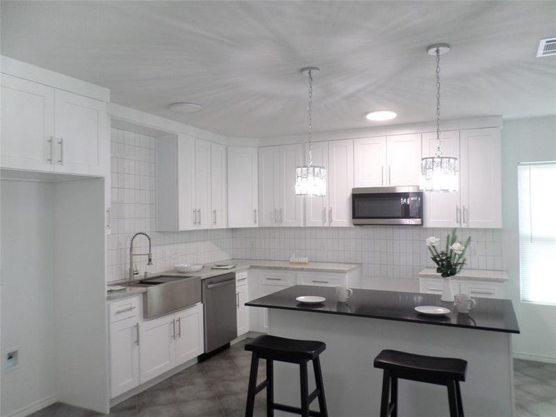 Kitchen featuring white cabinetry, stainless steel appliances, a farmhouse sink, subway tile backsplash, and a central island with a dark countertop