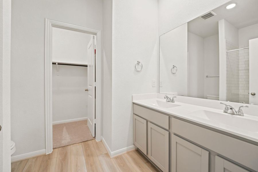 Double vanities with sleek countertops flank a spacious walk-in closet in this modern bathroom.