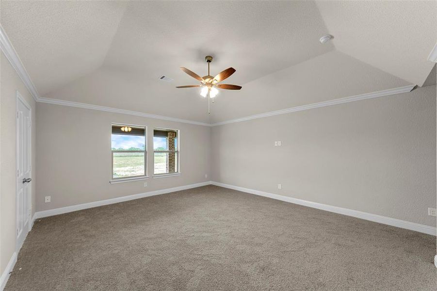 Spacious room featuring vaulted ceilings, crown molding, a ceiling fan, and carpeted flooring