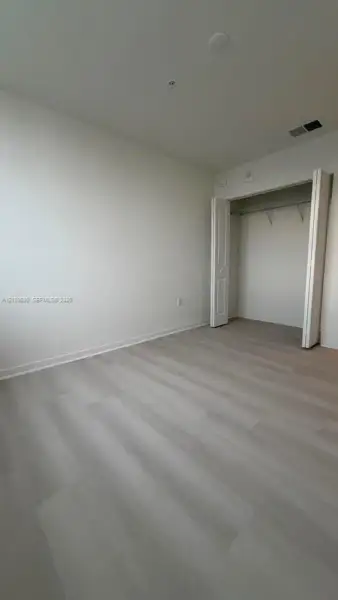 Neutral-toned wood-finish flooring, white walls, and a closet with bifold doors