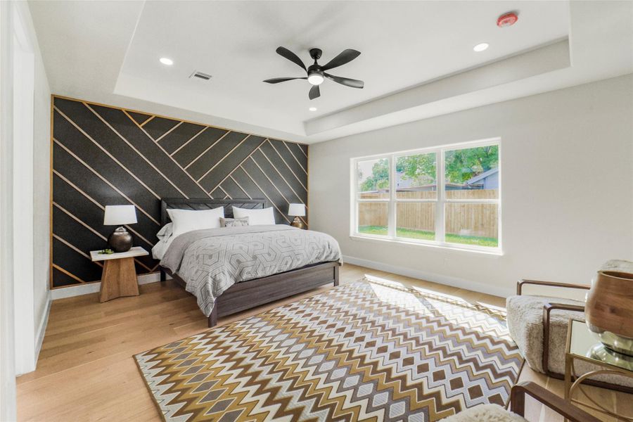 Spacious bedroom with modern geometric accent wall, large windows offering natural light, and stylish ceiling fan. It features a cozy bed, contemporary furniture, and a patterned rug on wooden floors.