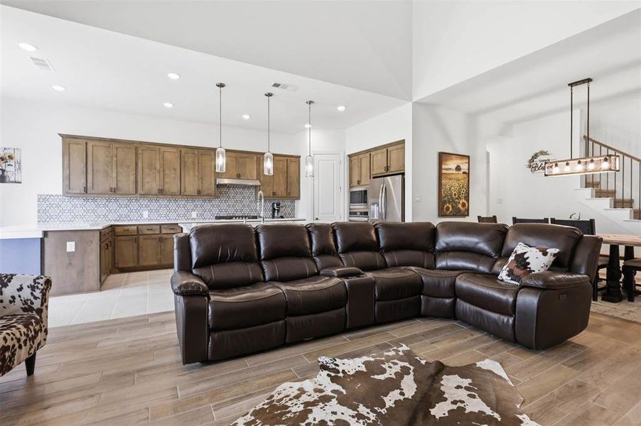 Open concept living area featuring wood-finish flooring, a kitchen with patterned tile backsplash, stainless steel appliances, and pendant lighting