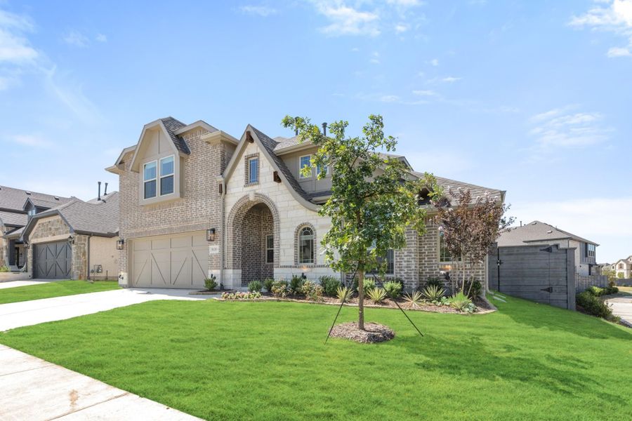 Two-story brick and stone home with arched entry, two-car garage, and landscaped front lawn
