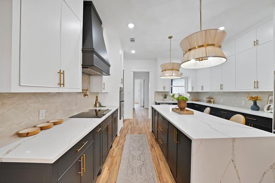 The kitchen features an expansive island with a white countertop and dark cabinetry, complemented by two stylish pendant lights