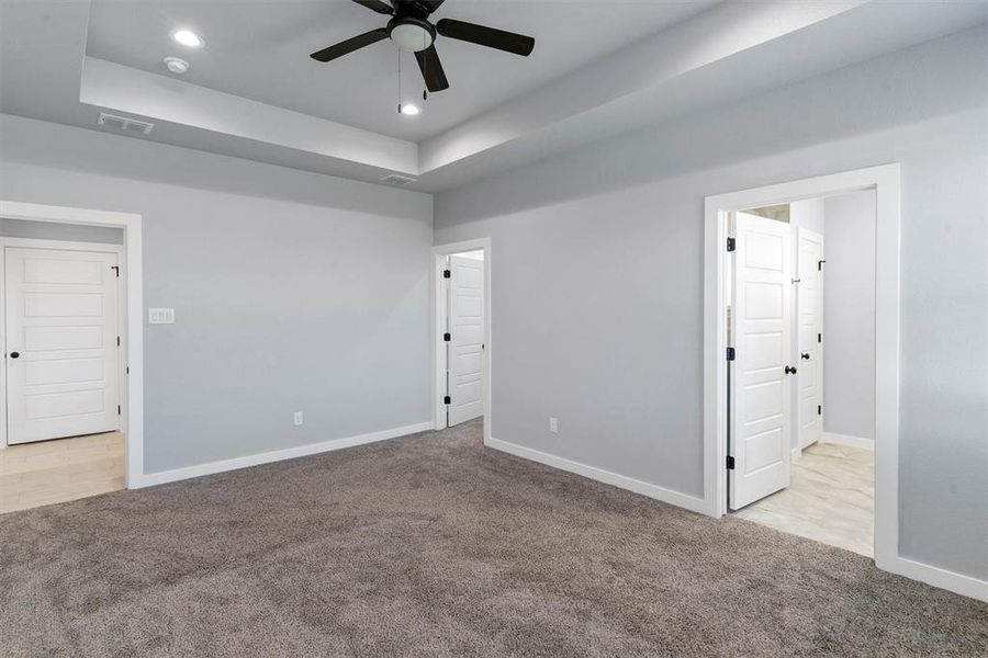 Spare room featuring ceiling fan, a raised ceiling, and light carpet