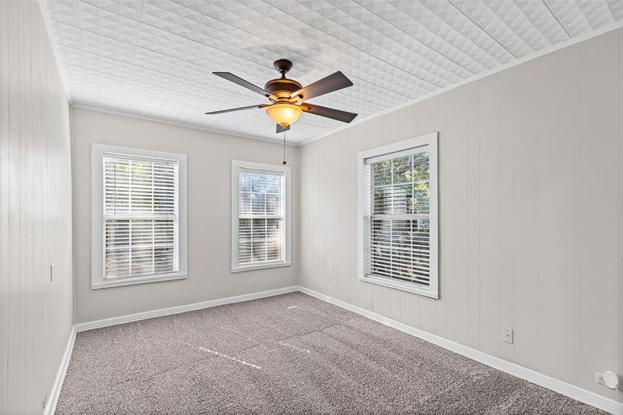 Empty room featuring carpet floors, crown molding, ceiling fan, and wooden walls