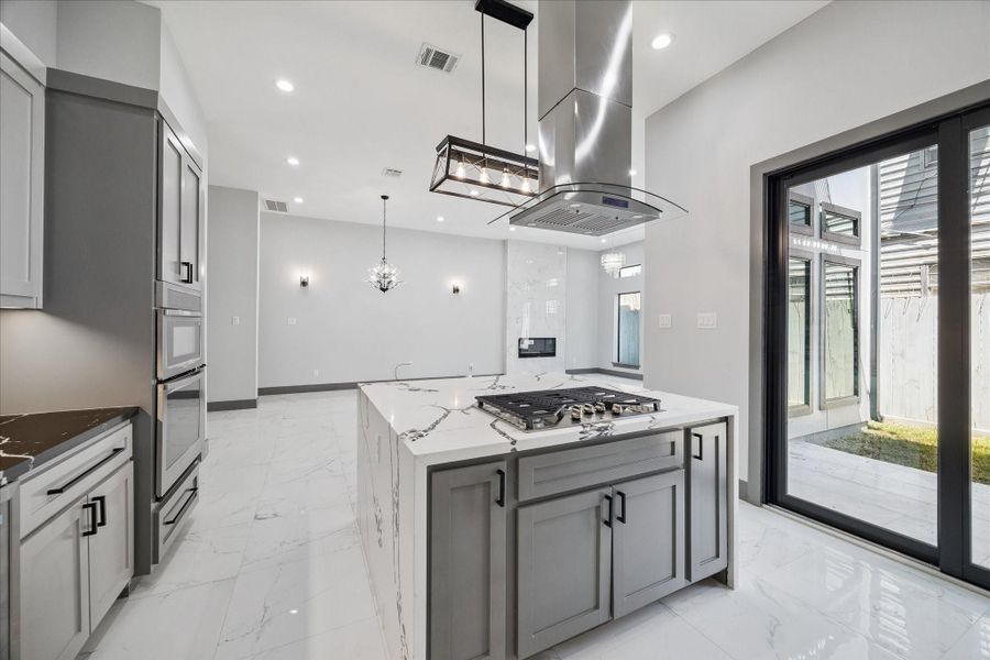Clean lines and thoughtful design define the kitchen, where a central island with cooktop and vent hood pairs with double ovens and custom cabinetry. Sliding glass doors open to the patio, enhancing both flow and functionality.