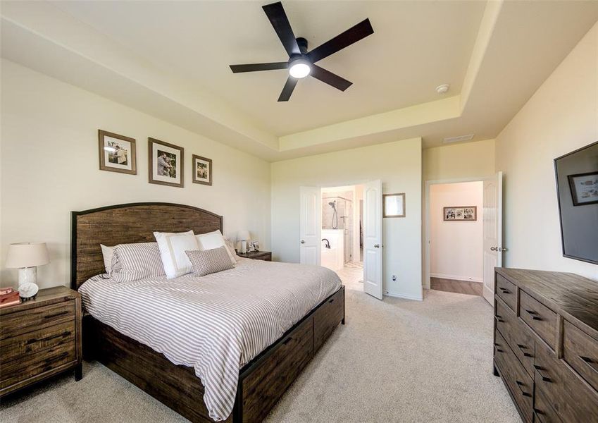 Bedroom featuring a raised ceiling, ensuite bathroom, light carpet, and ceiling fan