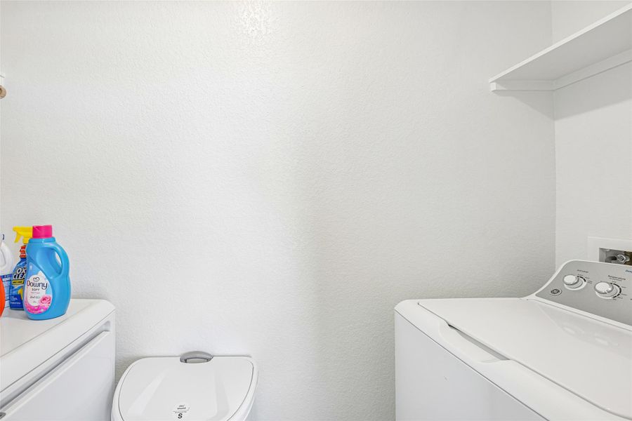 Dedicated laundry area featuring a built-in white shelf and white textured walls Dedicated laundry area featuring a built-in white shelf and white textured walls