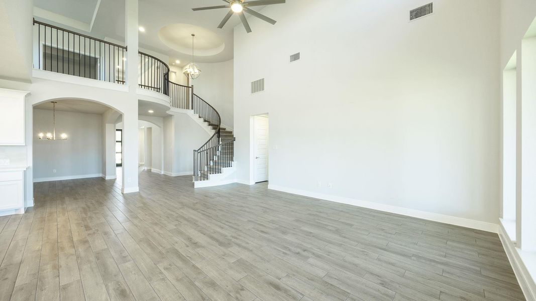 Unfurnished living room featuring a ceiling fan, stairway, a chandelier, light wood-style flooring, and a towering ceiling Unfurnished living room featuring a ceiling fan, stairway, a chandelier, light wood-style flooring, and a towering ceiling