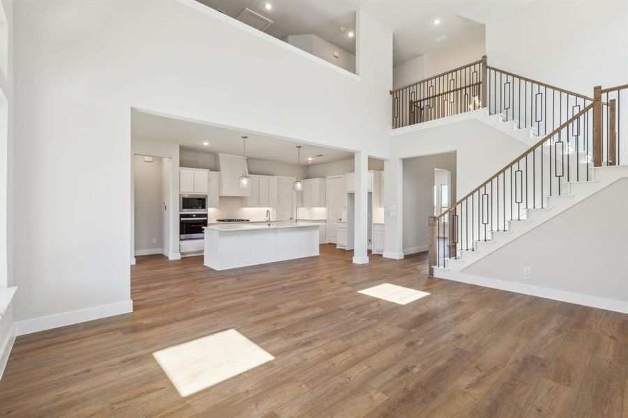 Unfurnished living room featuring sink, wood-type flooring, and a high ceiling