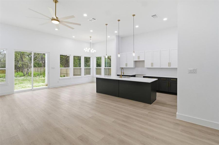 Kitchen with dark cabinetry, white cabinetry, a high ceiling, a kitchen island with sink, and recessed lighting