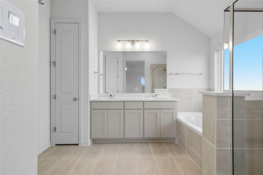 Full bath with a stall shower, a garden tub, plenty of natural light, double vanity, and lofted ceiling Full bath with a stall shower, a garden tub, plenty of natural light, double vanity, and lofted ceiling