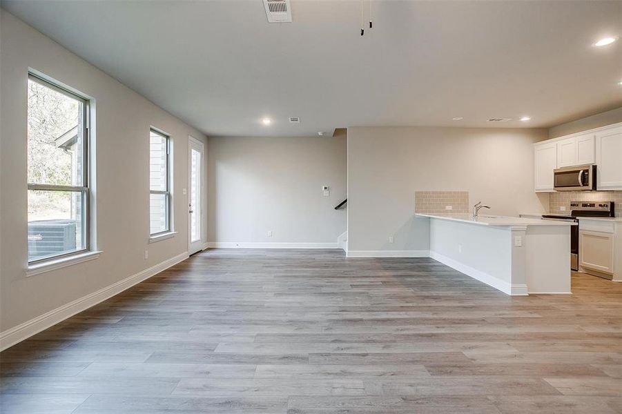 Kitchen with white cabinetry, backsplash, light hardwood / wood-style floors, and appliances with stainless steel finishes