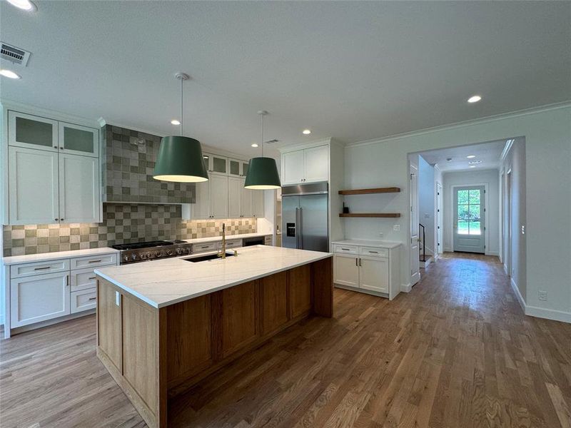 Kitchen with white cabinetry, light wood-type flooring, a center island with sink, and high end appliances