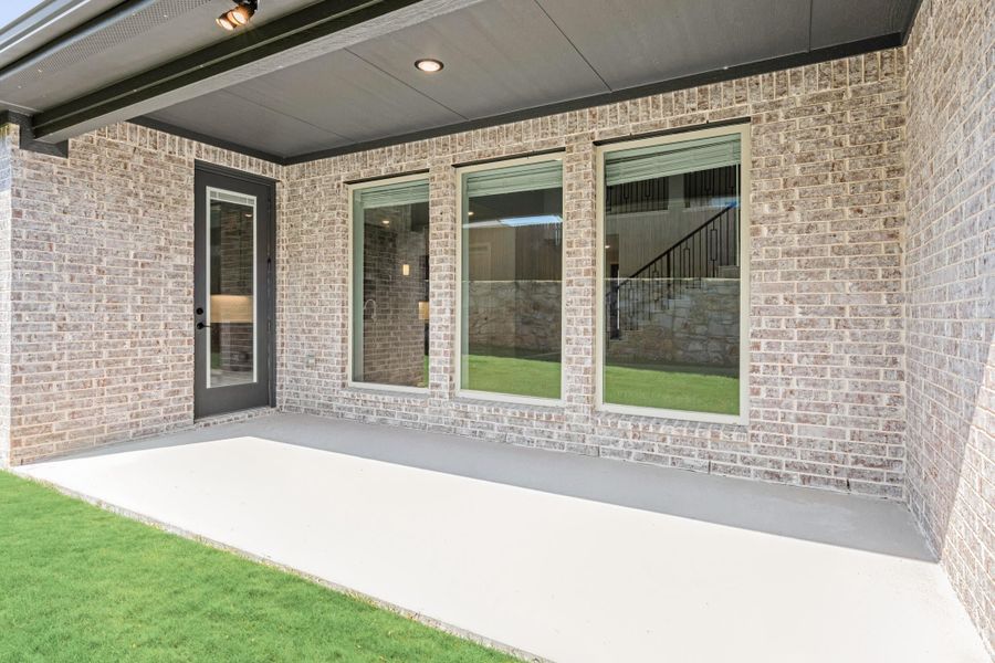 Covered back patio with concrete floor, brick exterior wall, large windows, and glass door leading inside
