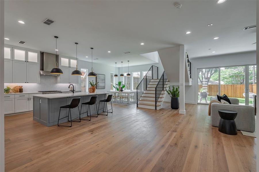 Kitchen featuring wall chimney range hood, light wood-type flooring, an island with sink, a breakfast bar area, and decorative light fixtures