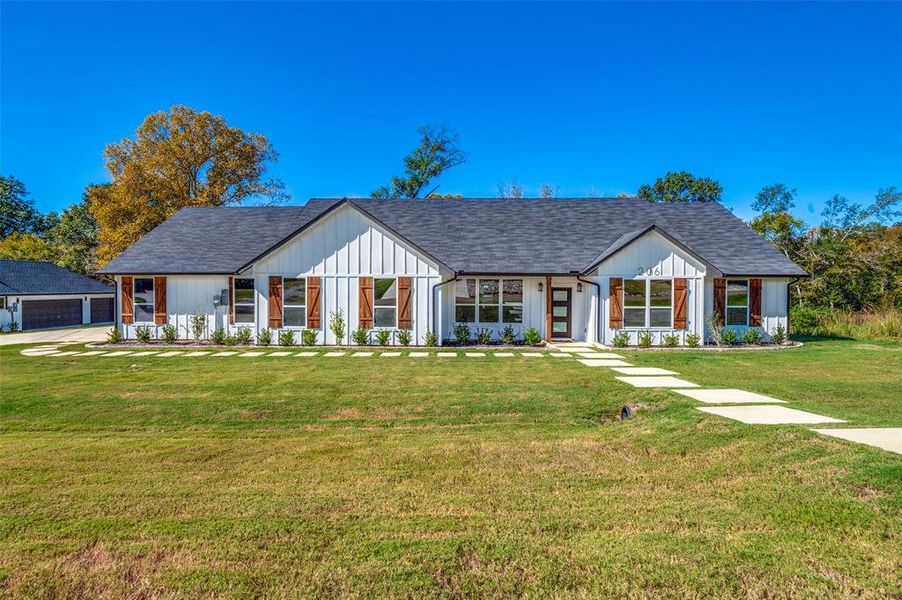 Modern farmhouse style home with a front yard, a porch, and a shingled roof