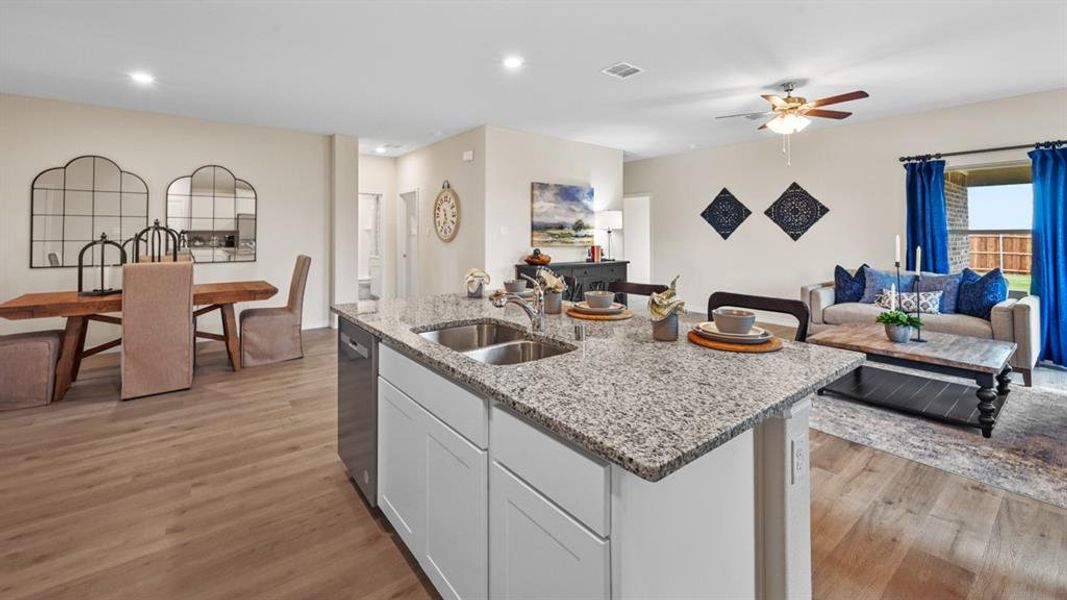 Kitchen with open floor plan, white cabinets, light stone countertops, light wood finished floors, and a center island with sink Kitchen with open floor plan, white cabinets, light stone countertops, light wood finished floors, and a center island with sink