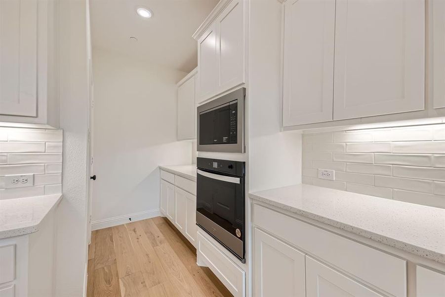 Kitchen with light hardwood / wood-style floors, black microwave, white cabinetry, light stone countertops, and stainless steel oven