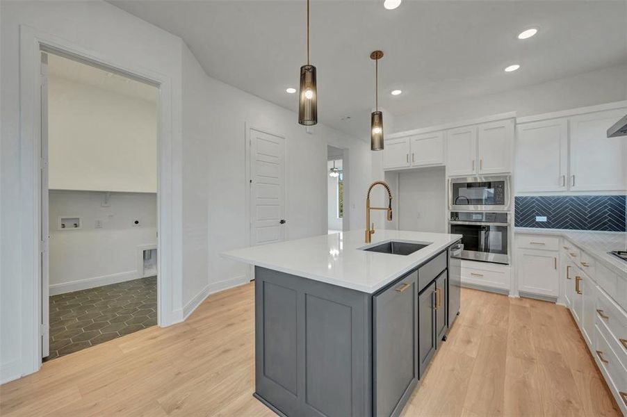 Modern kitchen featuring a central island with a dark gray base and white countertop, equipped with an undermount sink and a brass-finish faucet