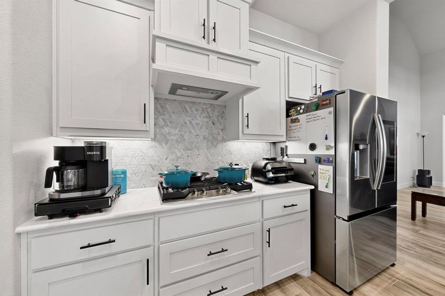 Kitchen with appliances with stainless steel finishes, decorative backsplash, light countertops, white cabinetry, and under cabinet range hood Kitchen with appliances with stainless steel finishes, decorative backsplash, light countertops, white cabinetry, and under cabinet range hood