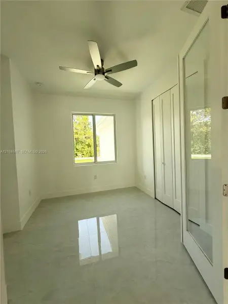 Room featuring polished tile flooring, a multi-blade ceiling fan, white bi-fold closet doors, and a glass-paneled entry door