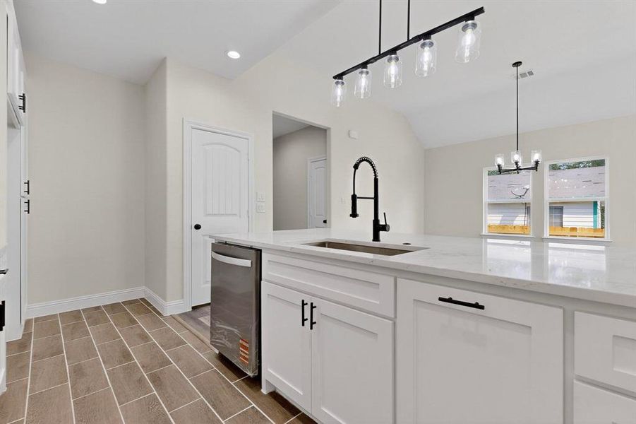 Kitchen with white cabinetry, light stone countertops, decorative light fixtures, stainless steel dishwasher, and lofted ceiling Kitchen with white cabinetry, light stone countertops, decorative light fixtures, stainless steel dishwasher, and lofted ceiling