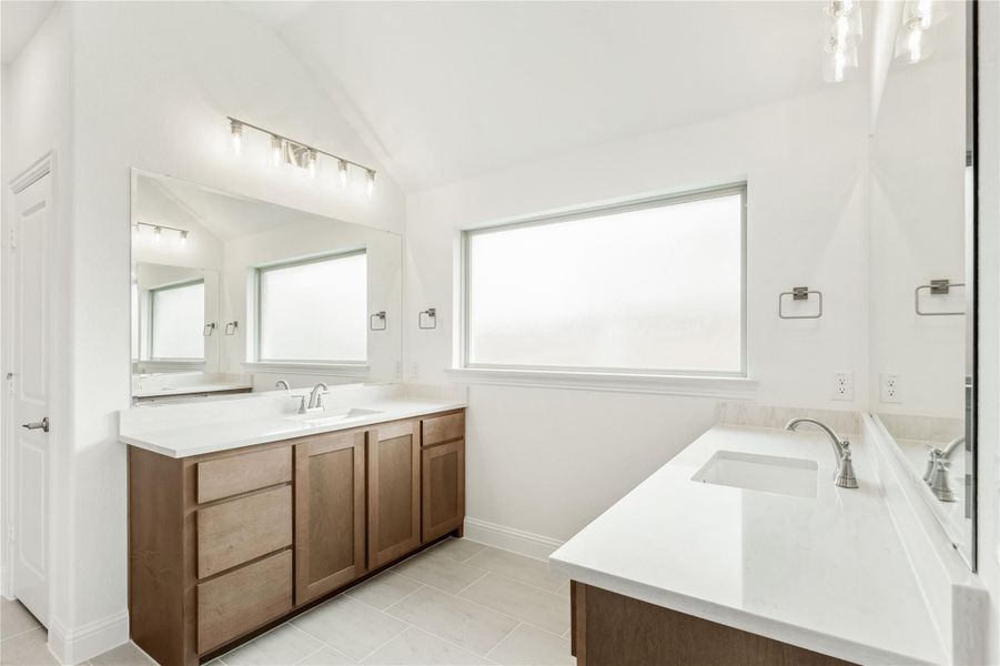 Bathroom with dual vanities, wood cabinets, white countertops, large mirror, and tile floors