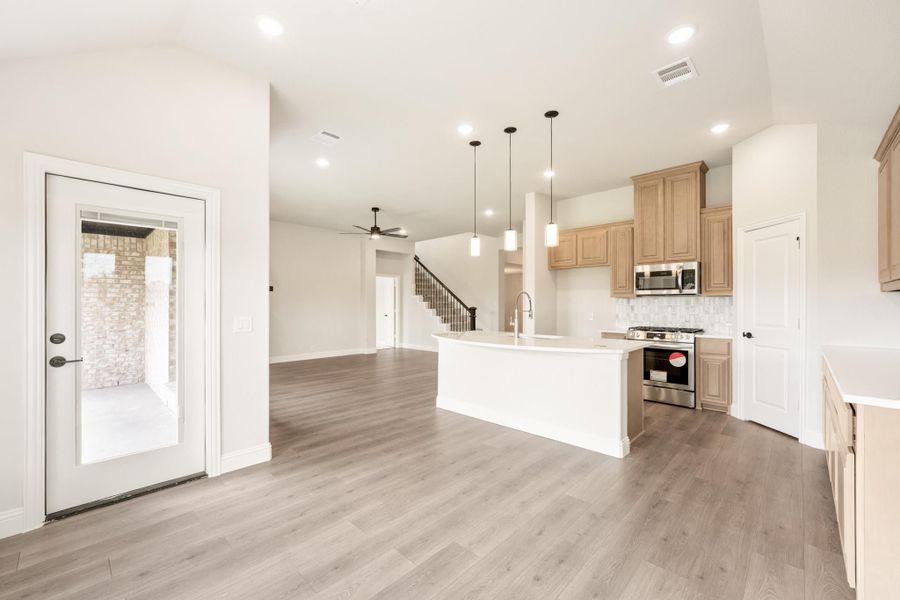 Open-concept kitchen with white island, tan cabinets, stainless appliances, and hardwood floors open to living area