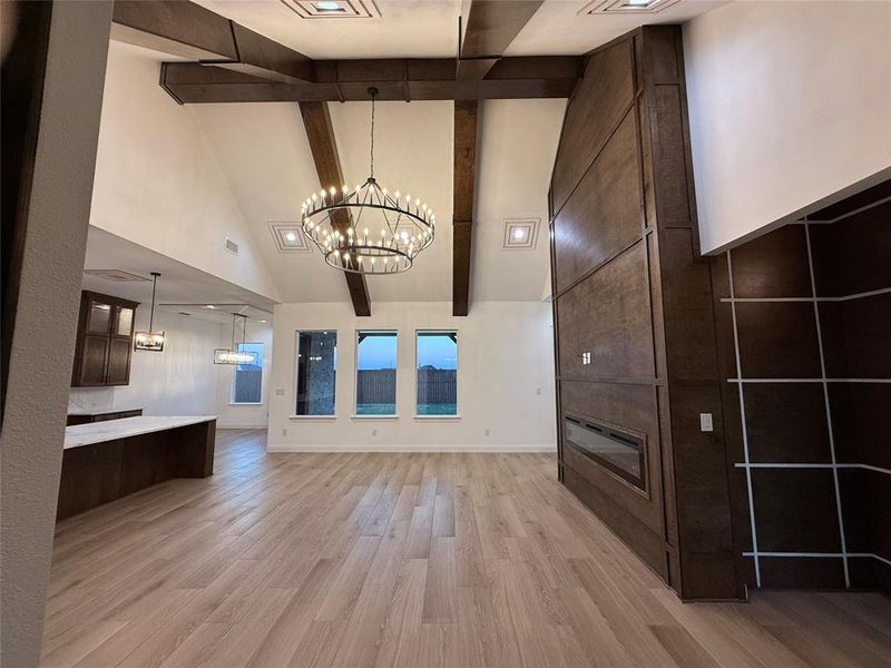 Unfurnished living room with beam ceiling, light wood-style floors, high vaulted ceiling, a chandelier, and a fireplace Unfurnished living room with beam ceiling, light wood-style floors, high vaulted ceiling, a chandelier, and a fireplace
