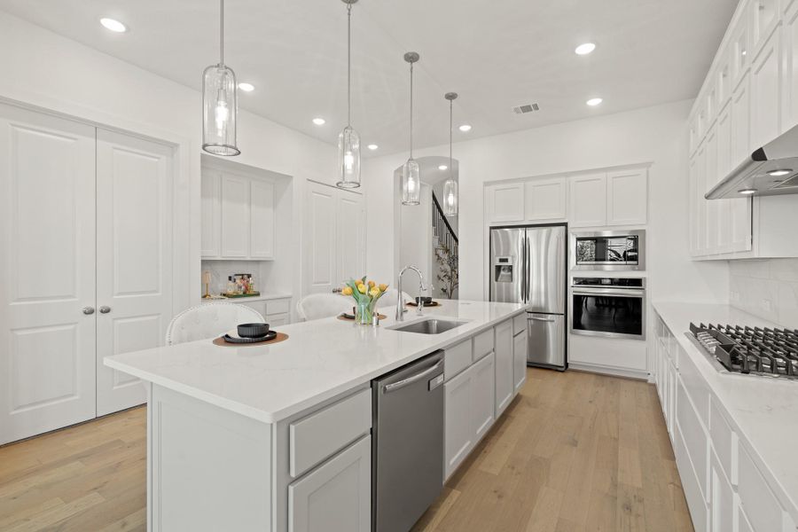This spacious kitchen features high ceilings, white cabinets, quartz countertops, SS appliances, modern tile backsplash and recessed lighting with additional custom pendant lighting.