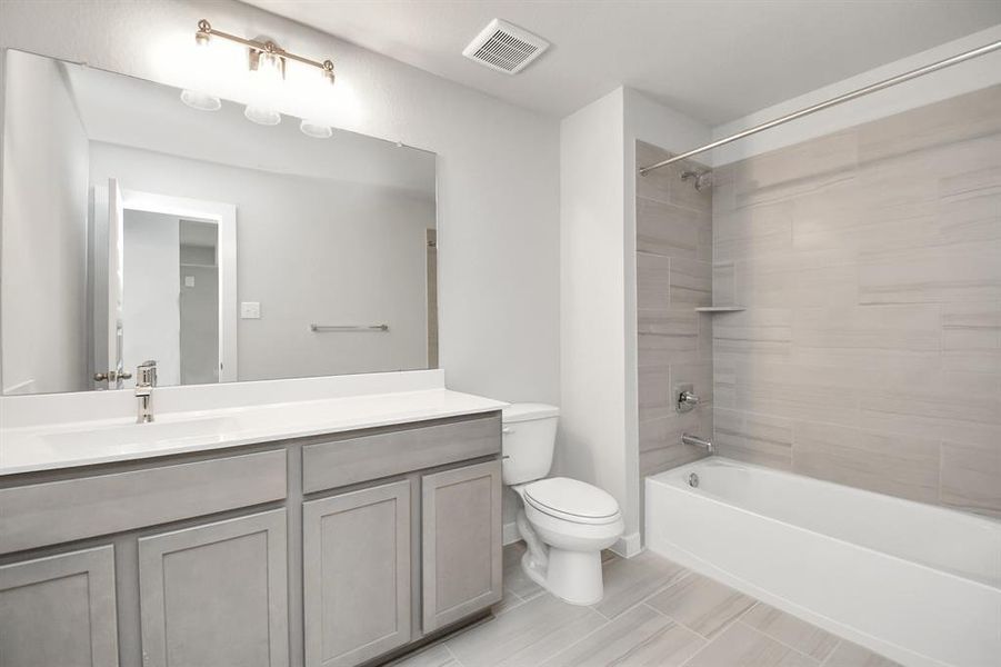 Secondary bath features tile flooring, bath/shower combo with tile surround, light stainedwood cabinets, beautiful light countertop.