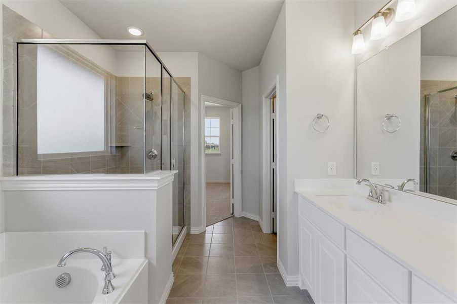Bathroom featuring a built-in tub, separate glass-enclosed shower with tile surround, dual vanity with white cabinetry, light-colored countertops, and tile flooring Bathroom featuring a built-in tub, separate glass-enclosed shower with tile surround, dual vanity with white cabinetry, light-colored countertops, and tile flooring