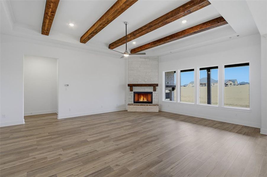 Unfurnished living room featuring a stone fireplace, recessed lighting, light wood-style flooring, a ceiling fan, and beam ceiling