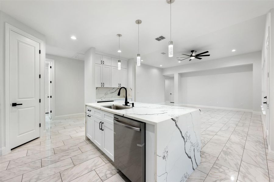 Kitchen featuring dishwasher, an island with sink, light marble finish flooring, pendant lighting, and light stone counters