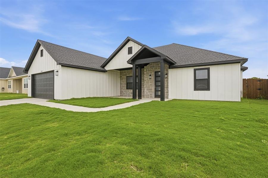 Modern ranch home featuring white board and batten siding, stone facade accents, a dark gray roof, and a two-car garage with a textured door