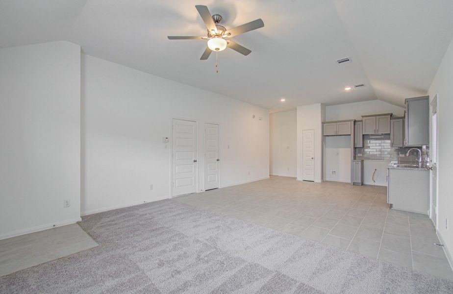 Spacious open-concept living area with fresh carpet and tile flooring, modern kitchen with sleek cabinetry, stainless steel appliances, and a ceiling fan for comfort.
