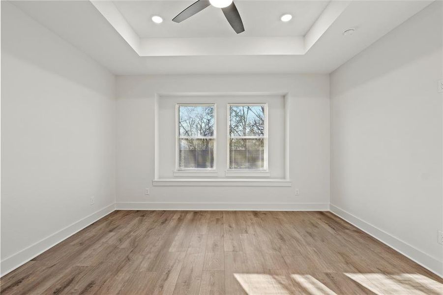 Empty room with a tray ceiling, baseboards, and wood finished floors