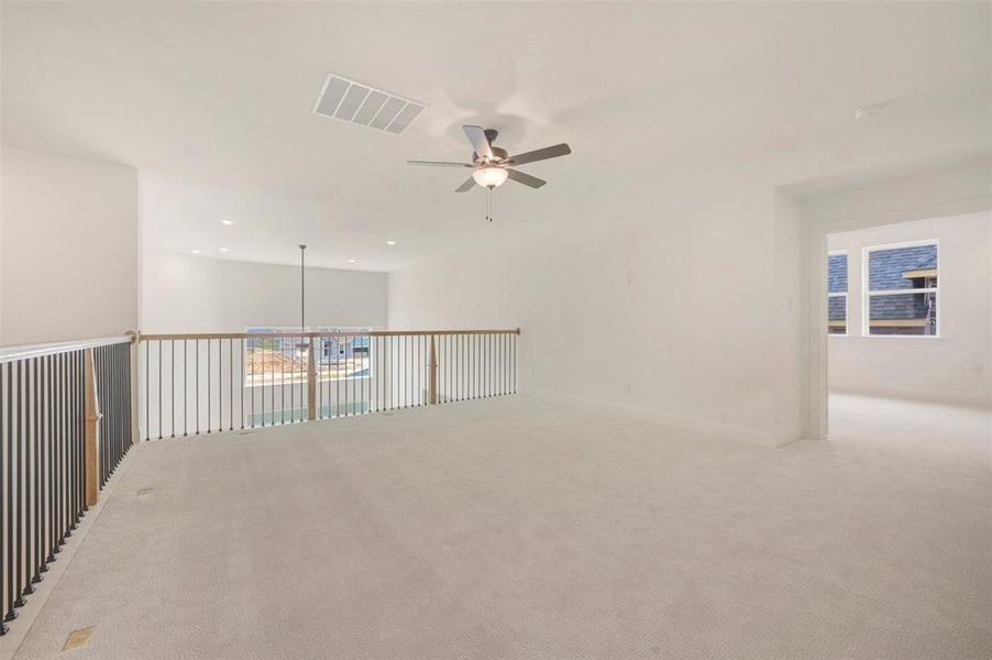 Spacious upper-level area featuring light-colored carpeting, a ceiling fan with integrated lighting, recessed lighting, a white painted ceiling, and a doorway leading to a separate room with windows