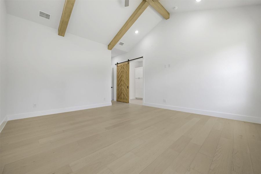Empty room featuring a barn door, light wood-type flooring, beam ceiling, recessed lighting, and high vaulted ceiling