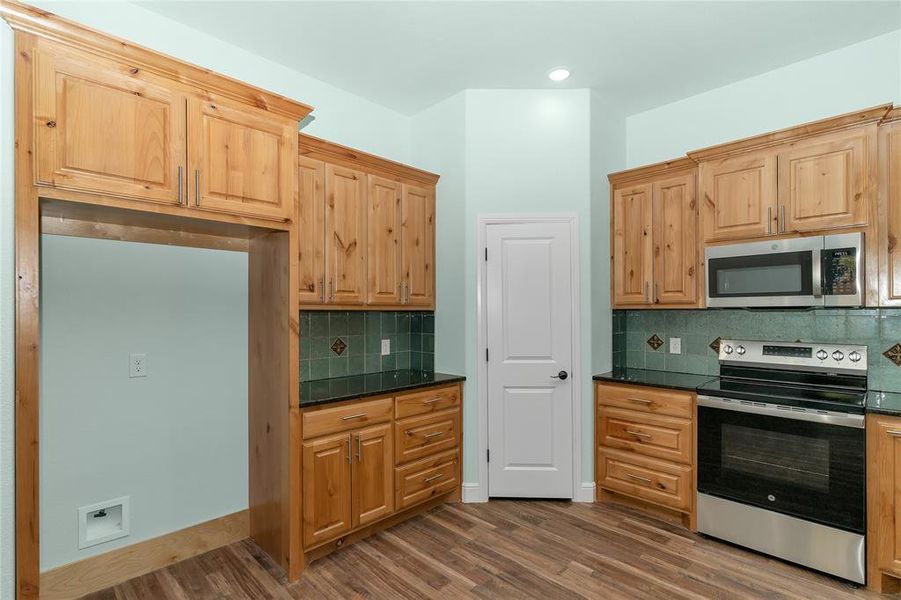 Kitchen featuring appliances with stainless steel finishes, backsplash, dark wood-style flooring, dark stone countertops, and recessed lighting