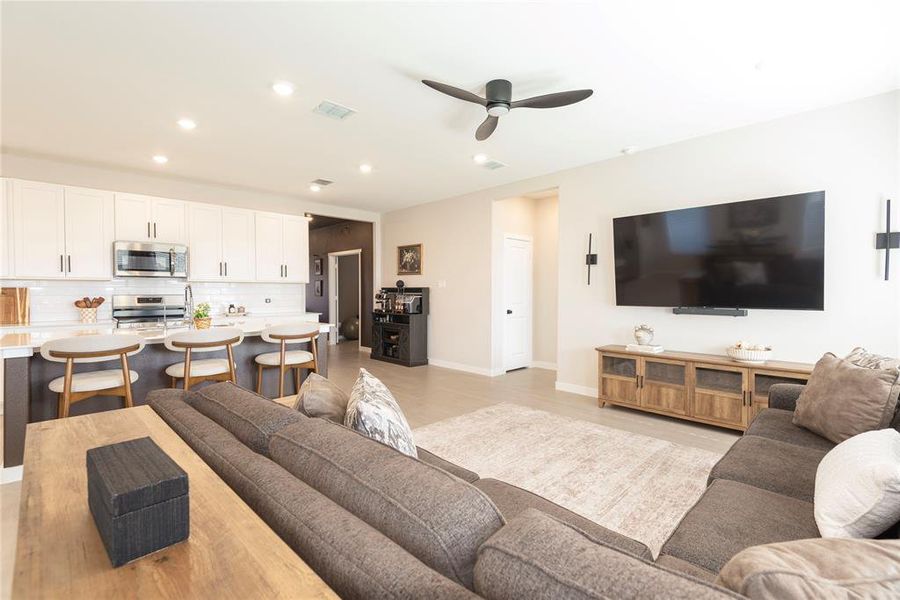 Open-concept living space featuring a kitchen with white cabinetry and stainless steel appliances, a breakfast bar with seating, recessed lighting, and a ceiling fan Open-concept living space featuring a kitchen with white cabinetry and stainless steel appliances, a breakfast bar with seating, recessed lighting, and a ceiling fan