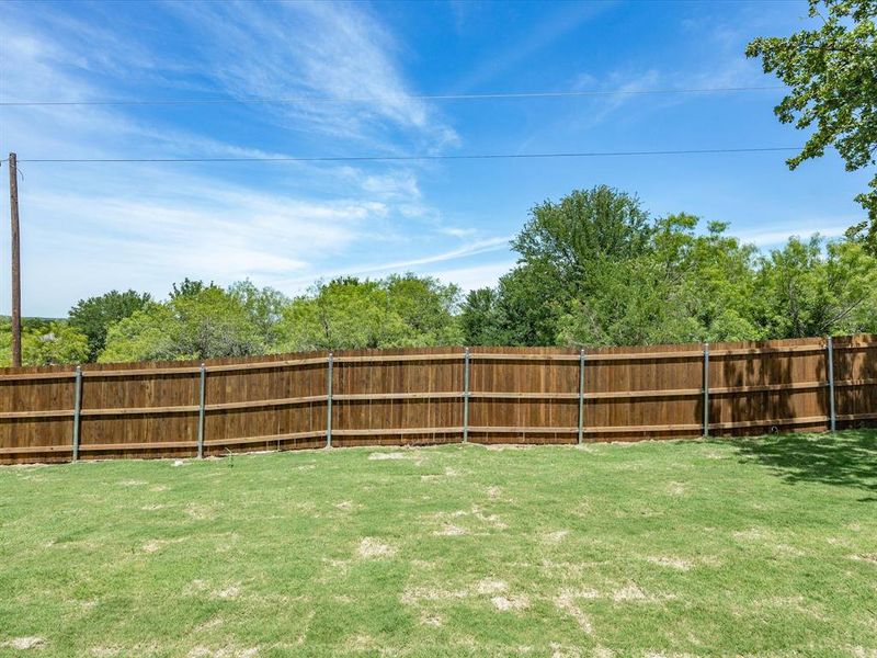 Expansive backyard featuring a manicured lawn and a privacy fence with wood panels and metal posts Expansive backyard featuring a manicured lawn and a privacy fence with wood panels and metal posts