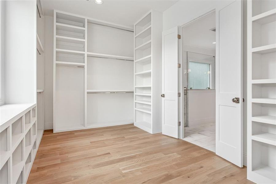 Primary walk in closet with custom shelving, built in mirror and large window