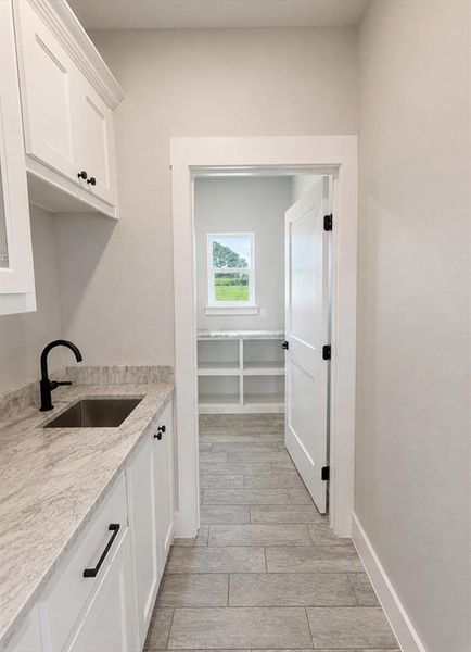 Utility room featuring white cabinetry, a stainless steel sink, and light-toned countertop Utility room featuring white cabinetry, a stainless steel sink, and light-toned countertop