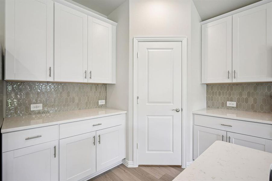 Kitchen featuring tasteful backsplash, white cabinets, light wood-type flooring, and light stone counters. USB ports in kitchen!  Oversized Pantry!